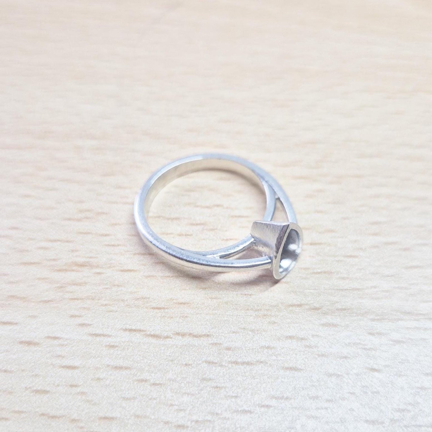 Silver round cathedral split bezel ring blank lying flat on a light wooden surface, showing the top of the empty open bezel and the entire ring.