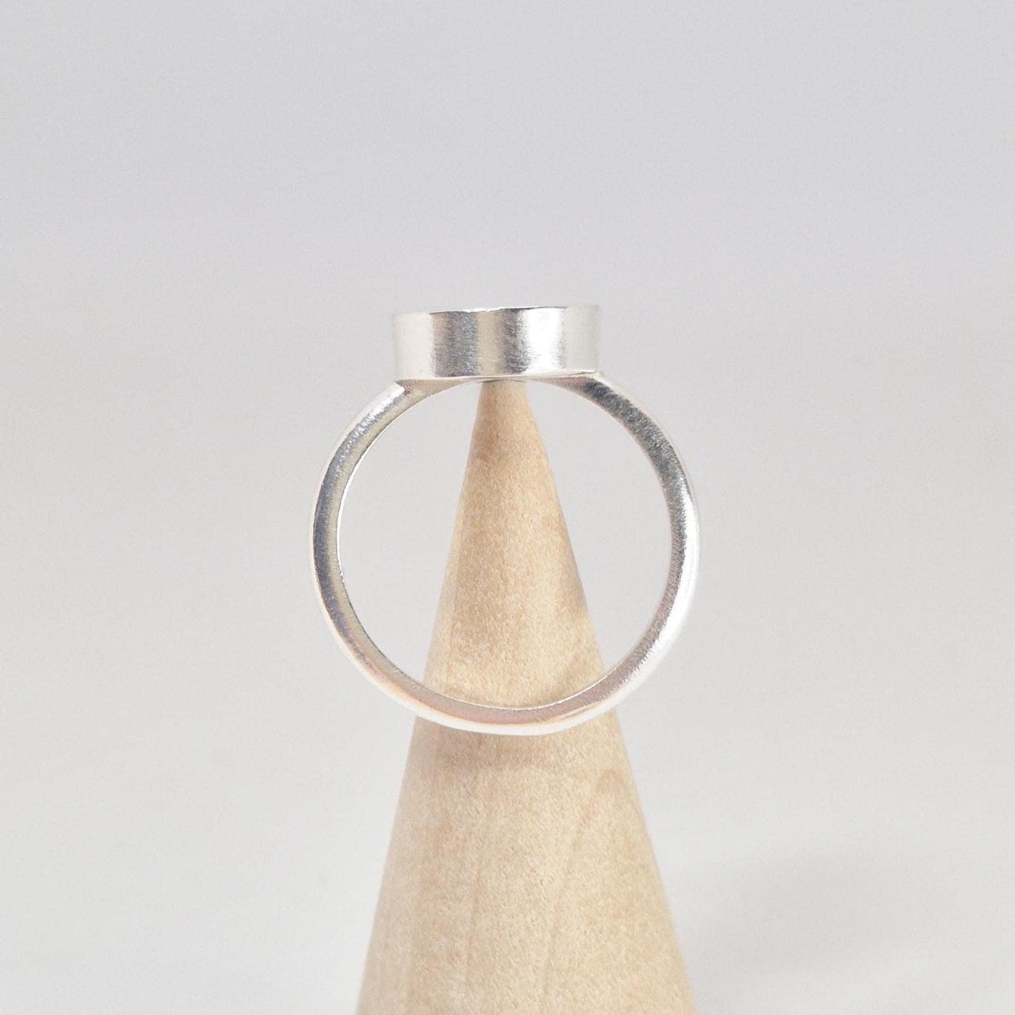Rear view of an empty sterling silver oval cabochon ring setting, displayed on a light wood conical stand.