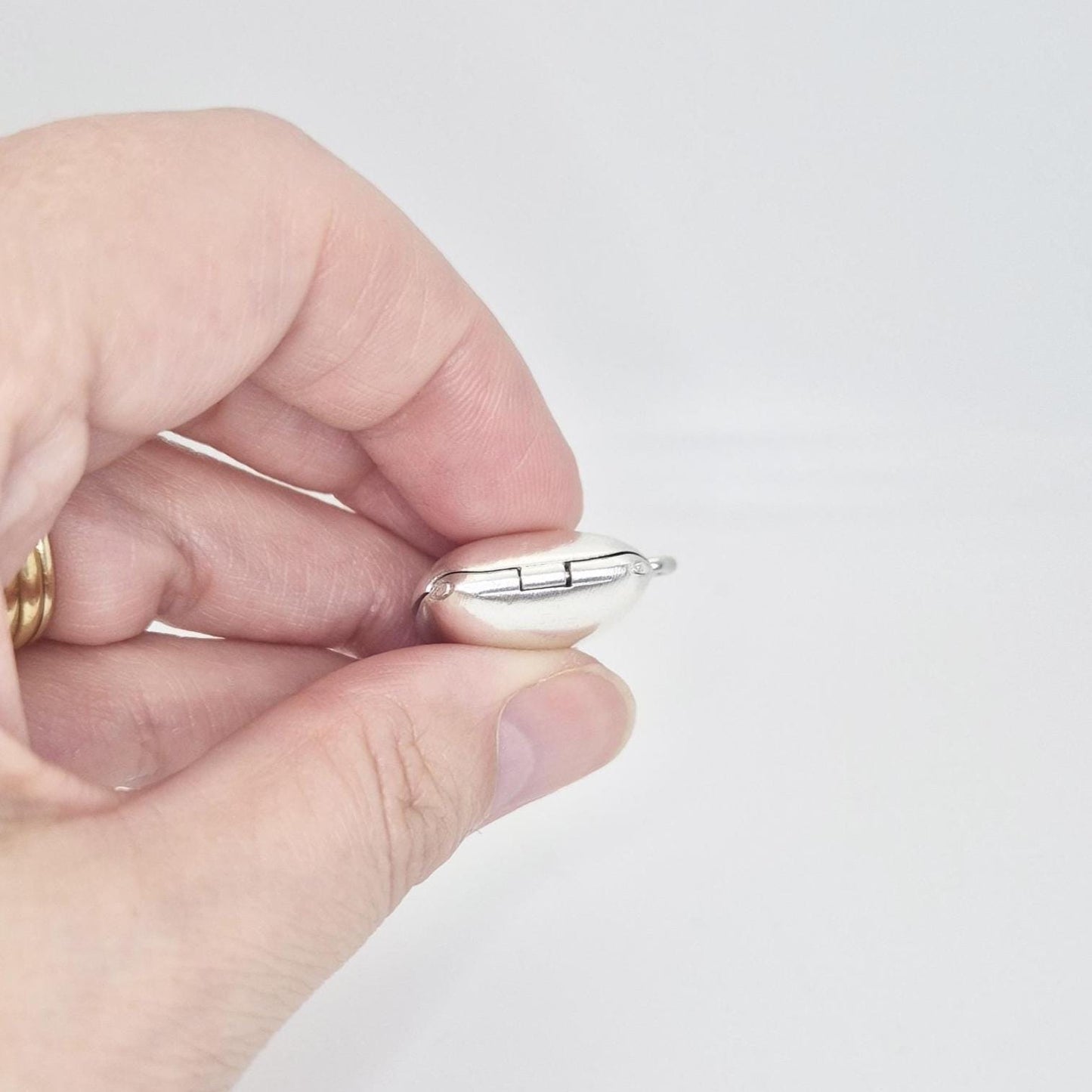 A hand holds a polished sterling silver square locket pendant, showing its hinged closure and the rounded edges from a side view.