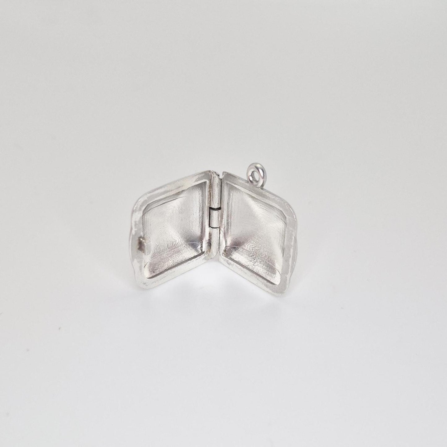 An open sterling silver square locket pendant, showcasing the hinge and the empty interior space of both sides, against a light grey background.