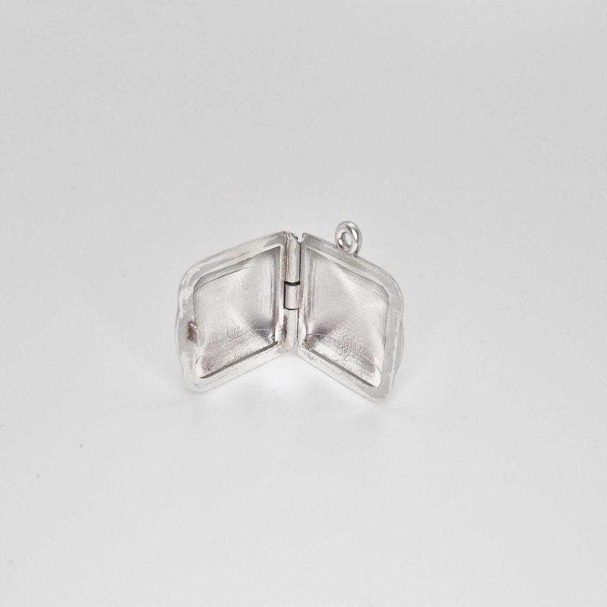 An open sterling silver square locket pendant, showcasing the hinge and the empty interior space of both sides, against a light grey background.
