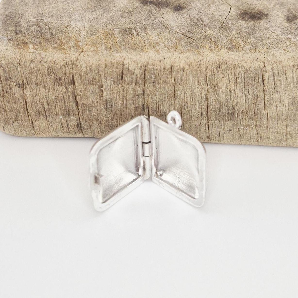 An open sterling silver square locket pendant resting on a textured, rustic wood block, showing its internal compartments.