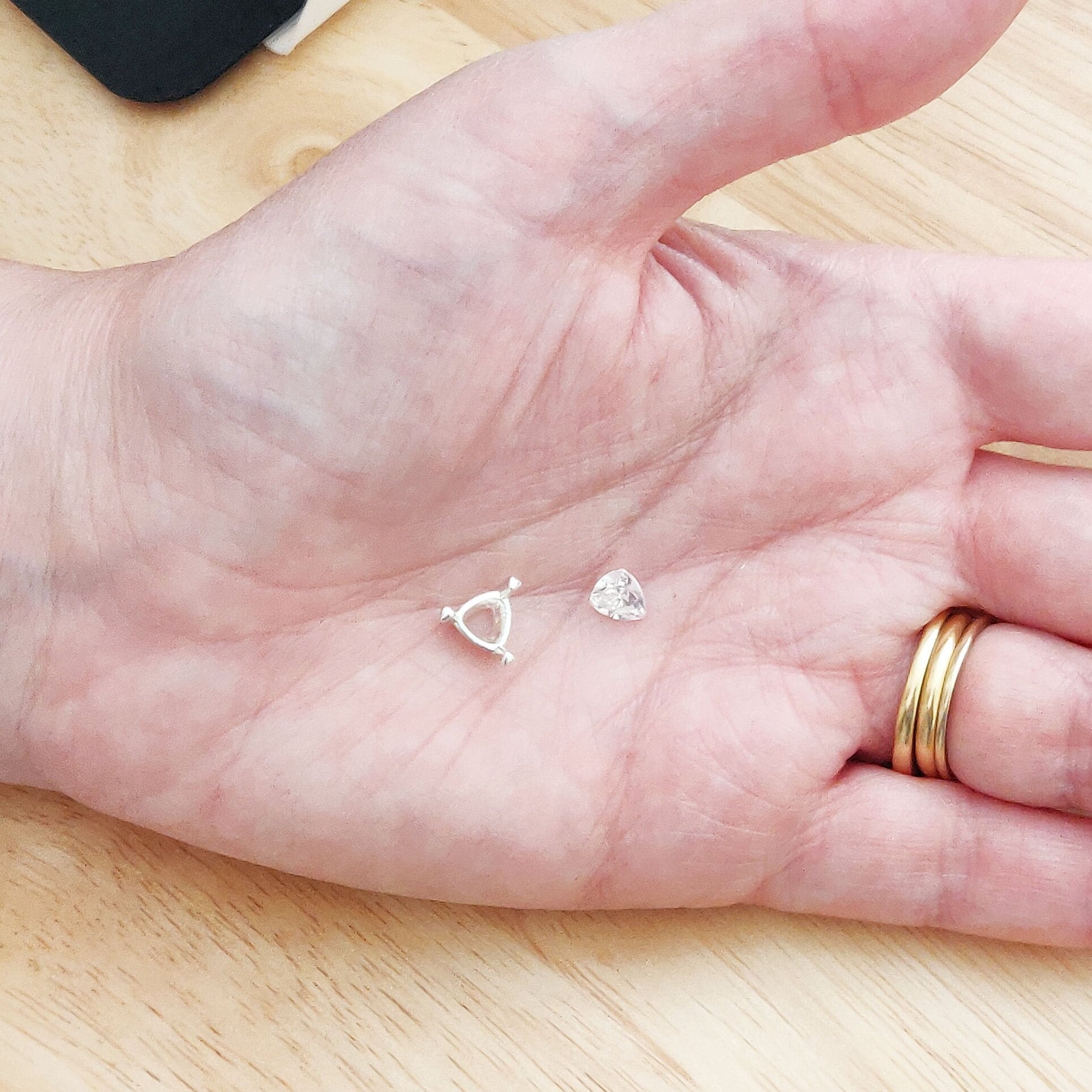 View of a silver trillion prong setting on a hand along with a gemstone for scale.