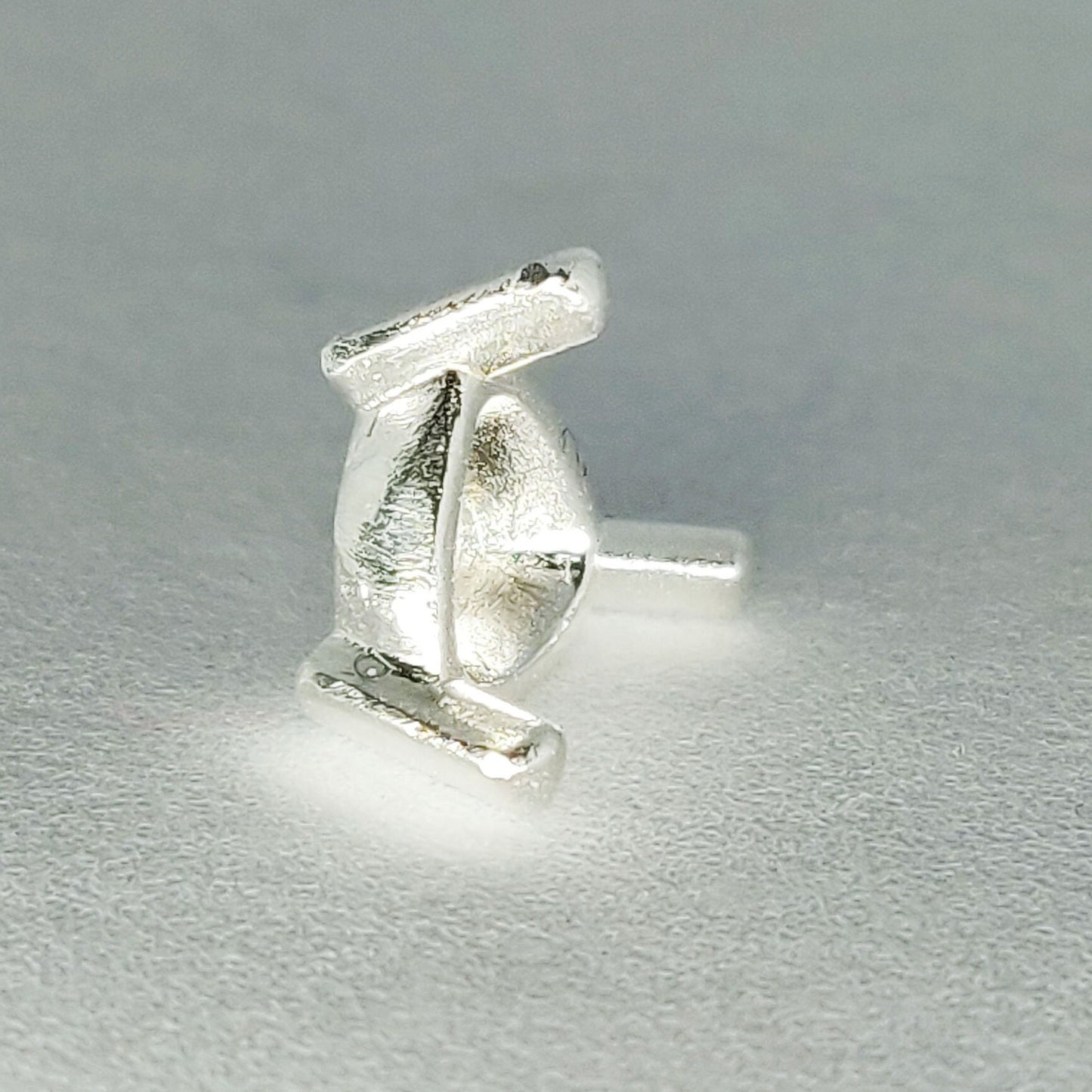 Profile view of a silver trillion prong setting on its side on a white background.