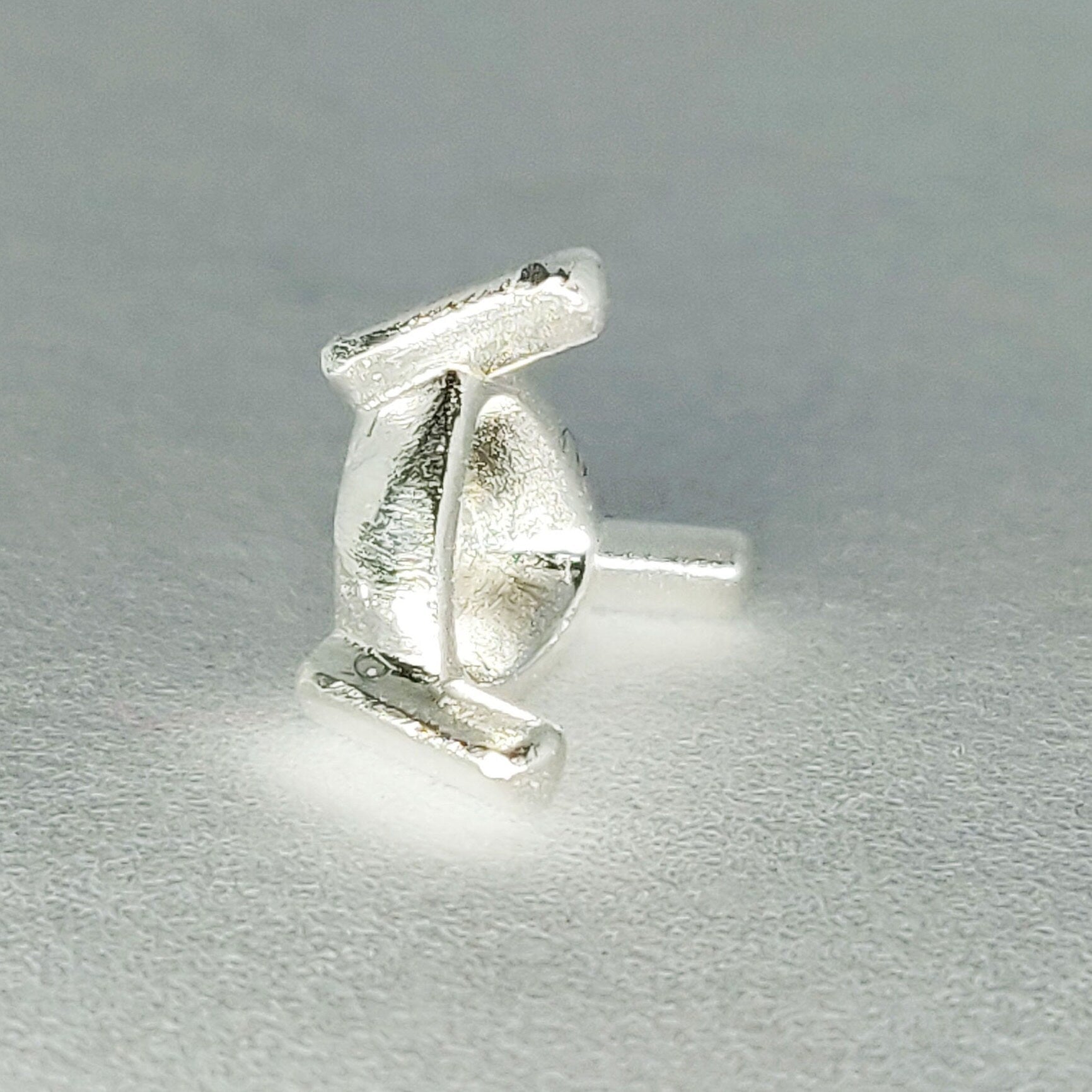 Profile view of a silver trillion prong setting on its side on a white background.