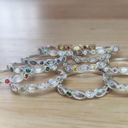 Selection of marquise and round cut eternity rings with different birthstones on a wooden background.