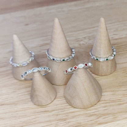 Selection of minimalist eternity rings with birthstones on wooden cones for display.