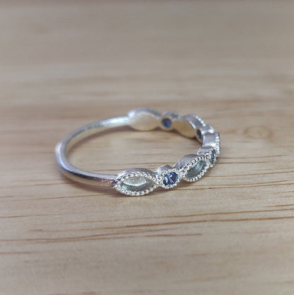 Side view of a silver eternity stacking ring with blue sapphires on a wooden table.
