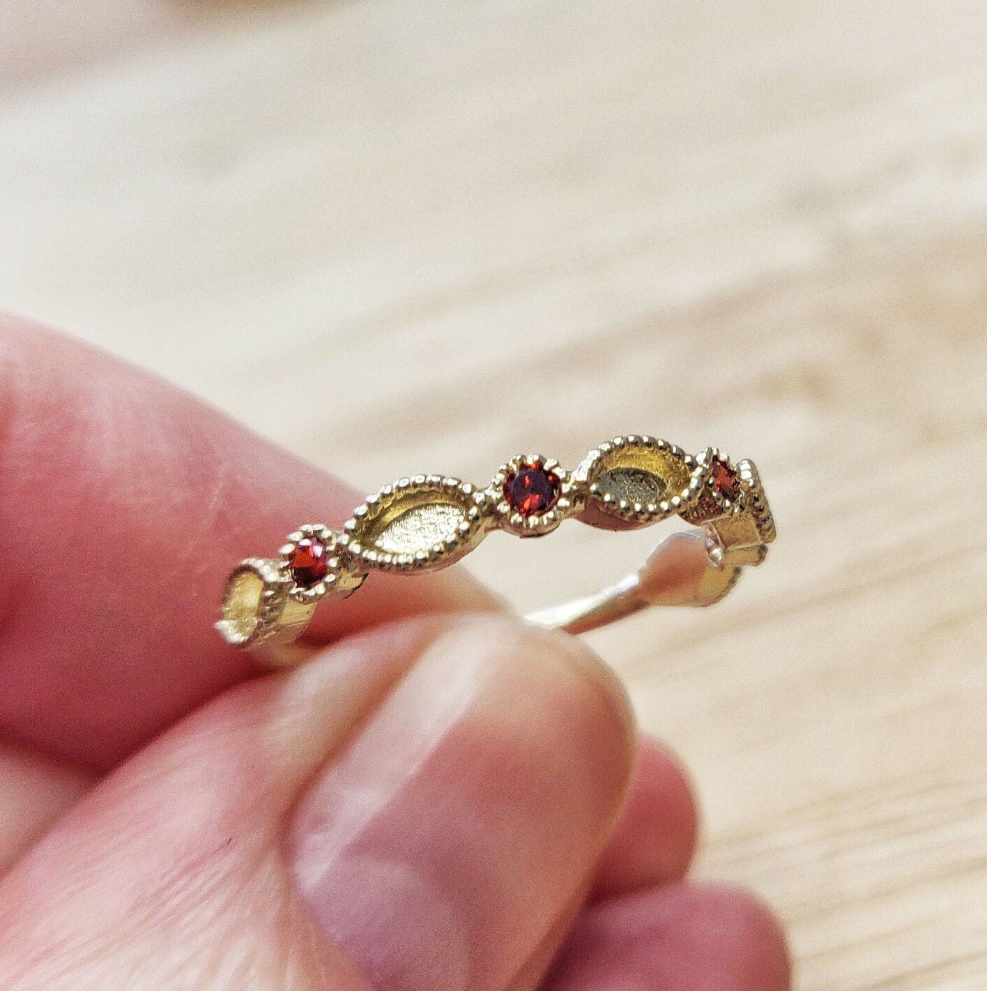 Gold and Red Cubic Zirconia Eternity Ring being held inbetween 2 fingers.