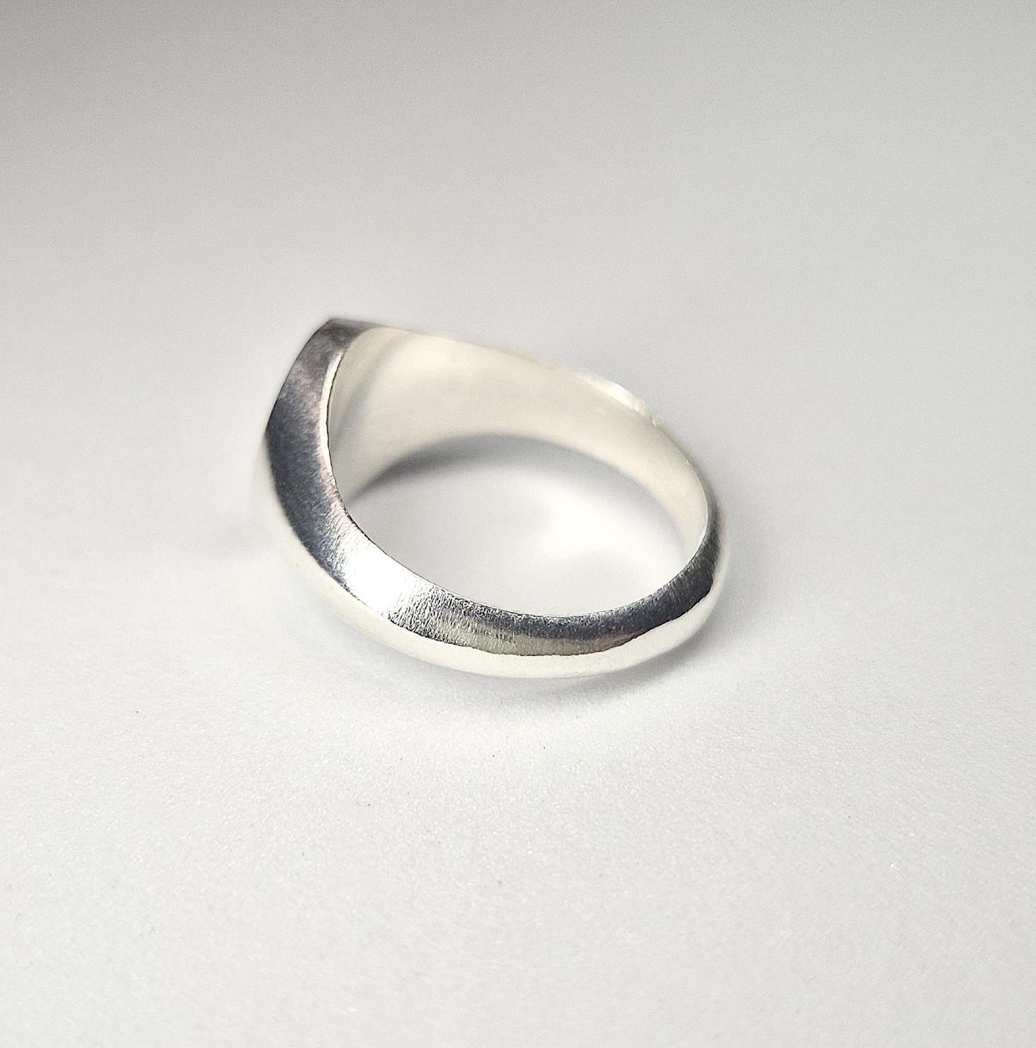 Through finger view of a silver signet ring on a white background.