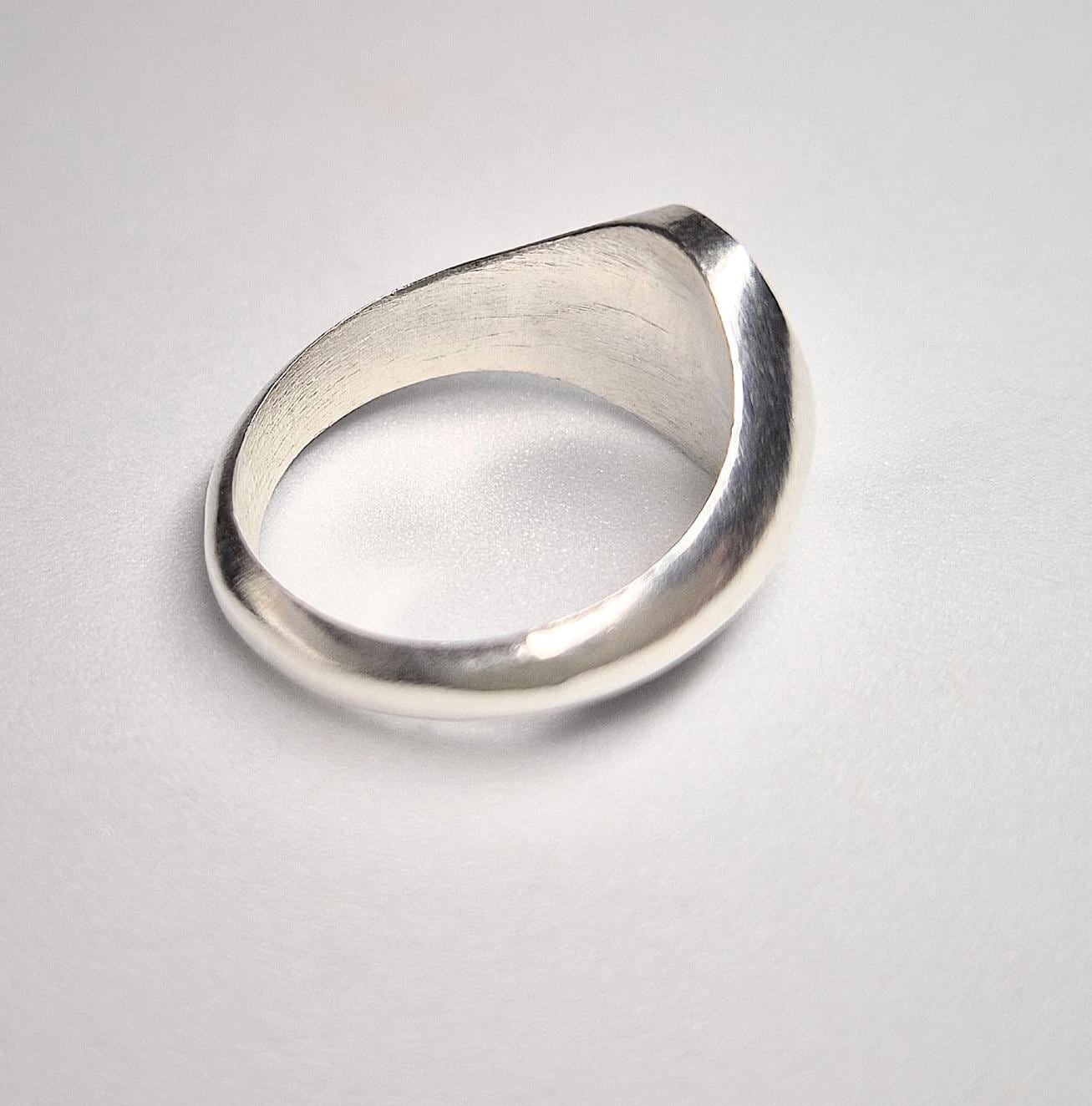 Bottom through finger view of an oval silver signet ring on a white background.