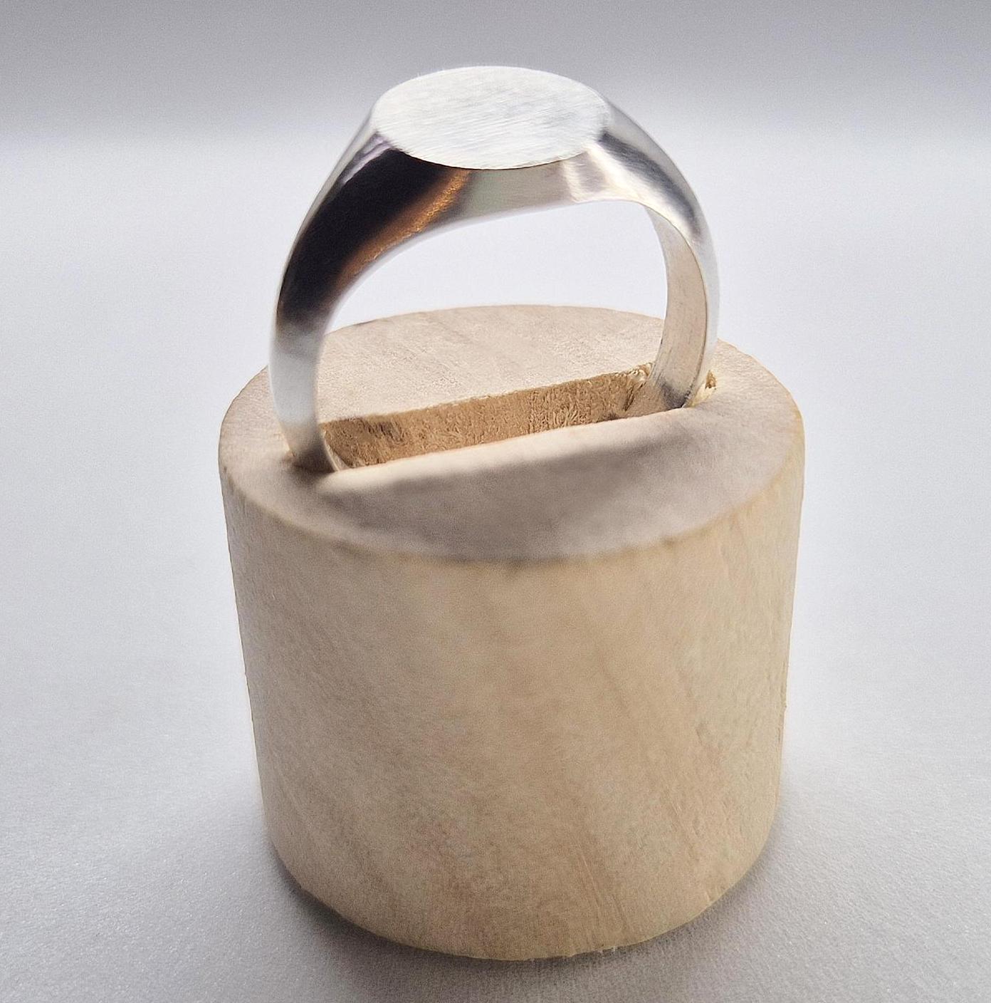 Oval silver signet ring in a wooden display stand.