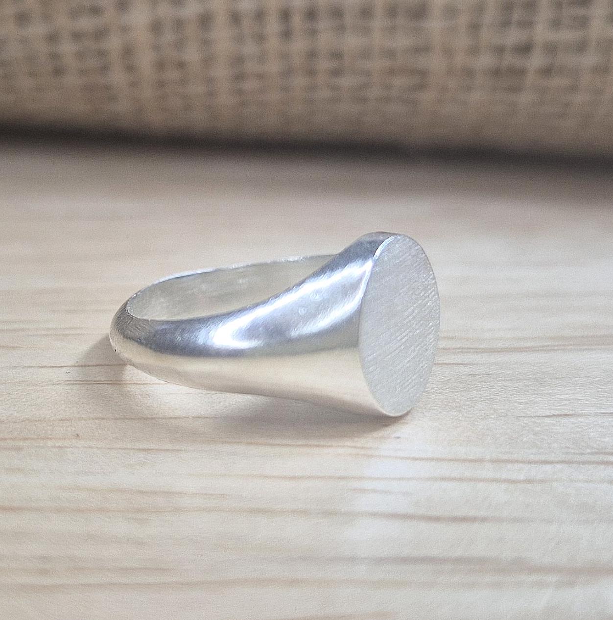 Side view of an oval silver signet ring on a desk.