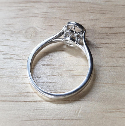 Silver cathedral shank ring with basket bezel on a wooden background.