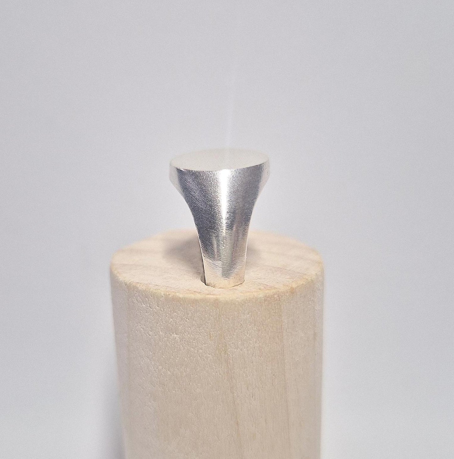 Side view of an oval silver signet ring in a wooden display stand.