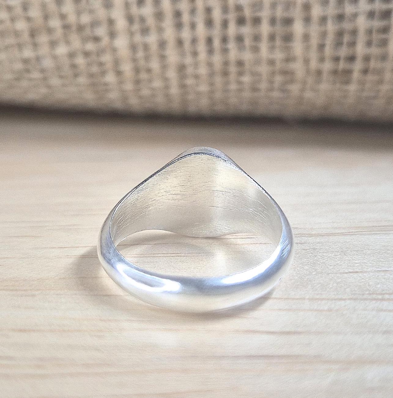 Rear view of an oval silver signet ring on a desk.