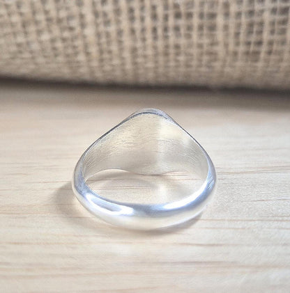 Rear view of an oval silver signet ring on a desk.