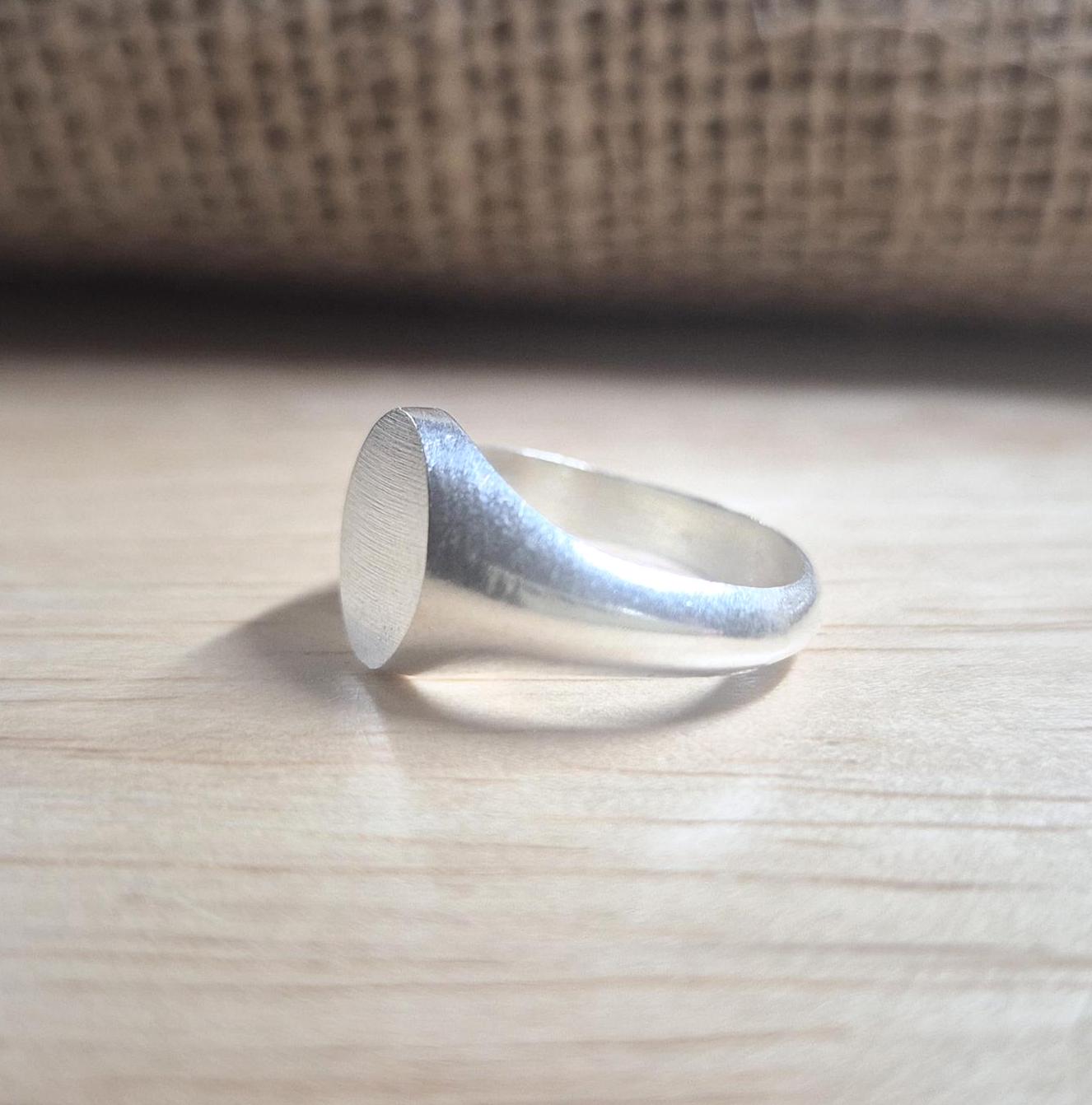 Side view of an oval silver signet ring on a desk.