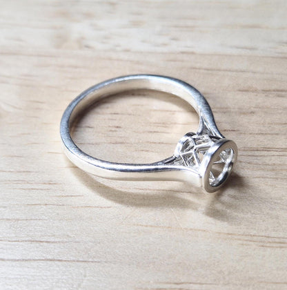 Silver cathedral shank ring with basket bezel on a wooden background.