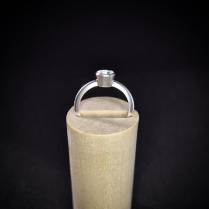 Empty Silver Bezel Ring in a Wooden Stand Against a Black Background.