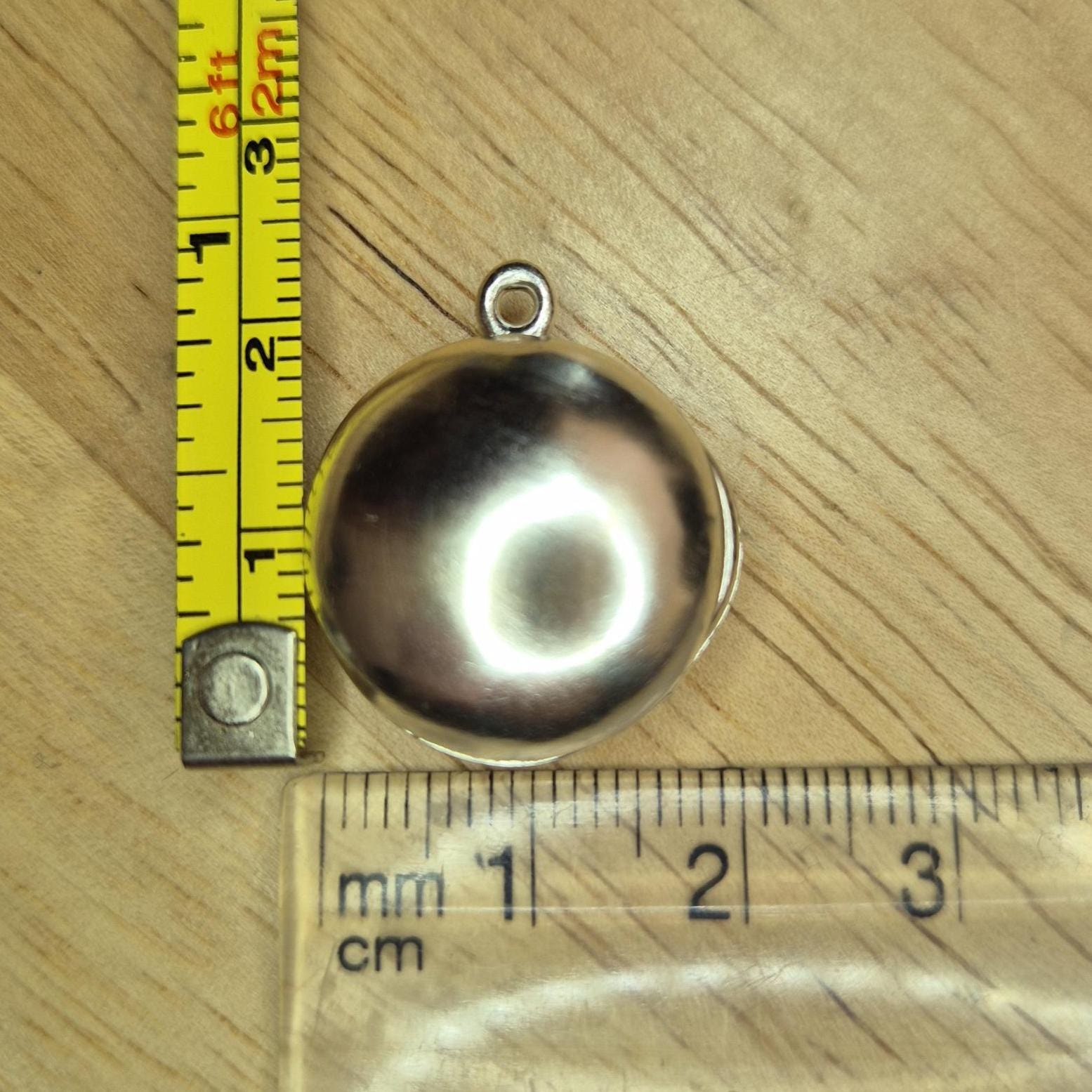Closed Round Silver Locket with Measuring Tape and Ruler for Scale.