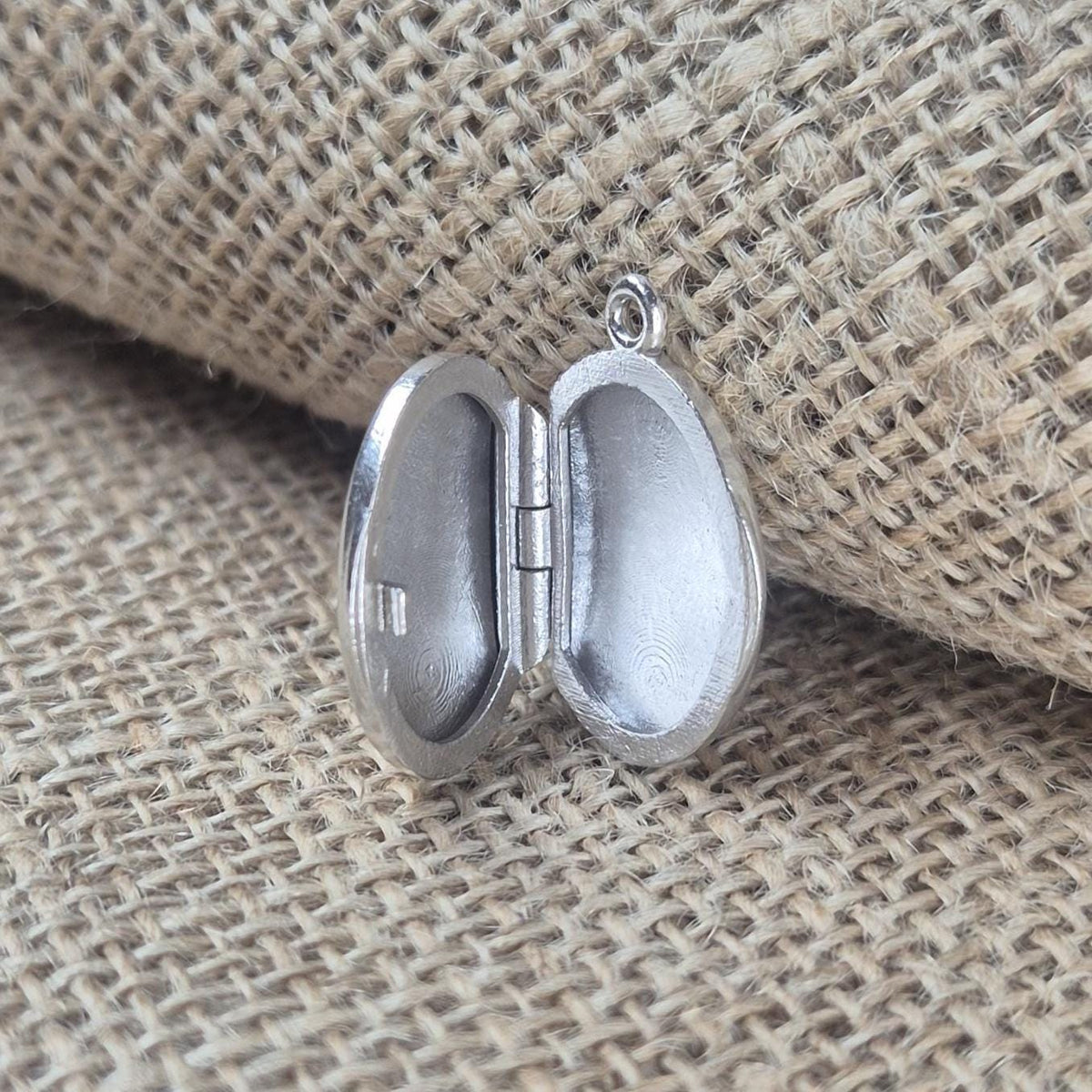 Open Oval Silver Locket Against a Jute Background.