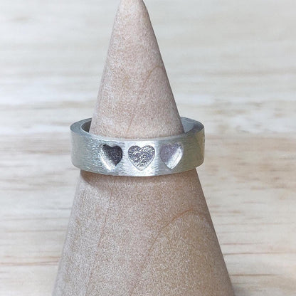 Three-heart silver ring displayed on a wooden ring cone, ideal for ashes or breastmilk resin fillings.