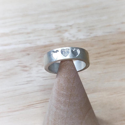Artisan silver band with recessed hearts on a cone stand, set against a light wood backdrop.