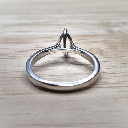 Flat lay of a silver cathedral shank ring blank with an empty 2-prong marquise setting, displayed on a light wooden surface.