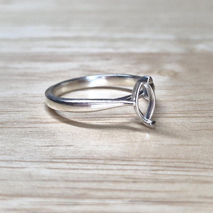 Side view of a delicate silver ring blank with cathedral-style shoulders and marquise setting, set on a pale wood background.