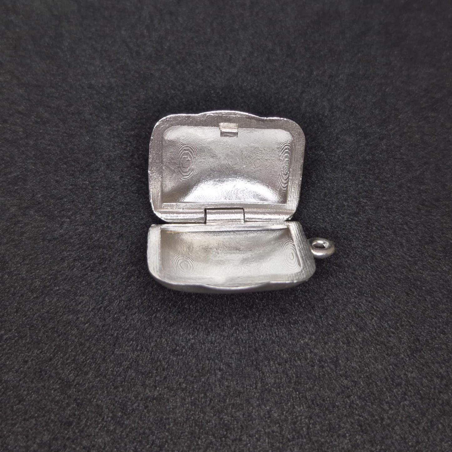 Sterling silver locket open flat on black background, clearly displaying both inner halves and hinge construction.