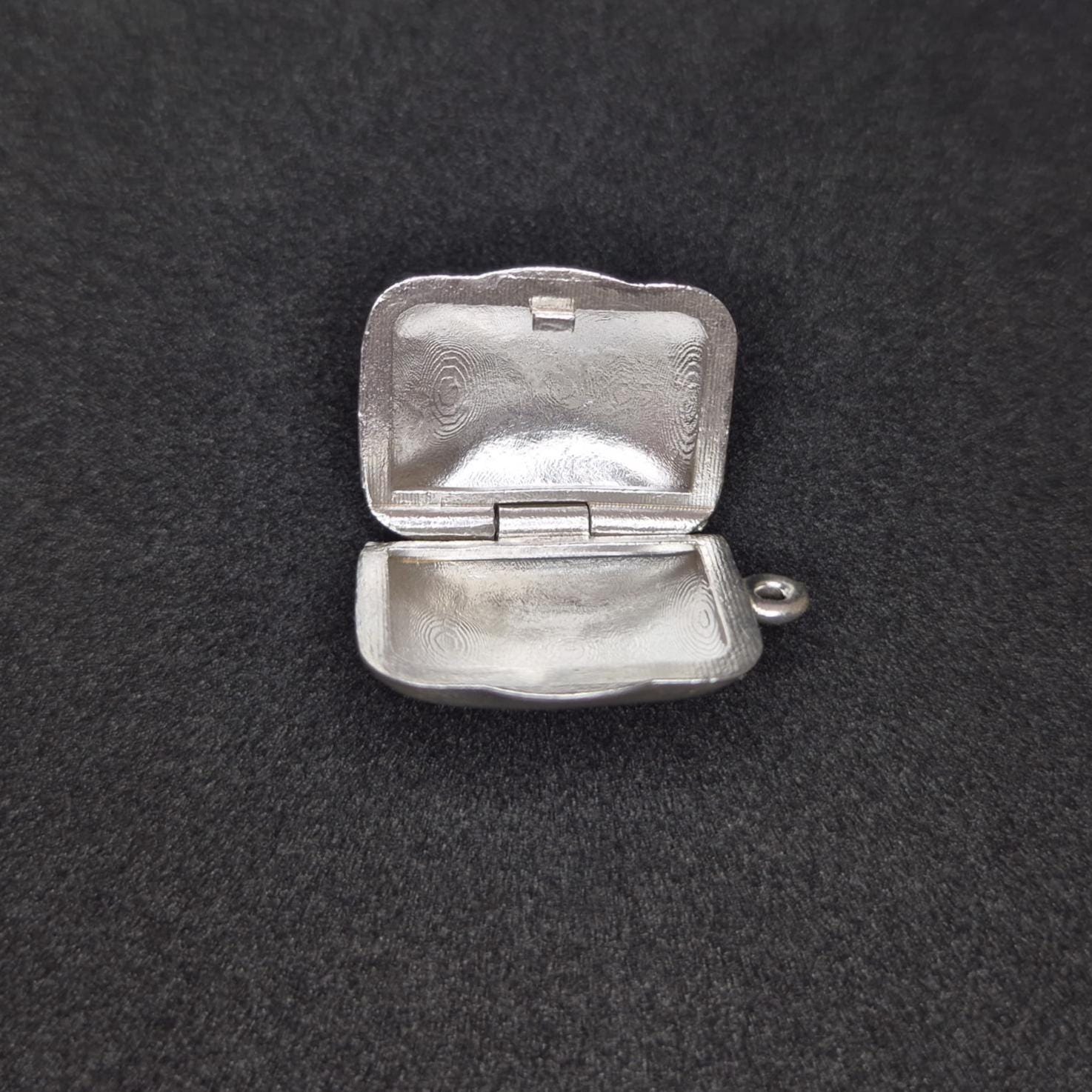 Sterling silver locket open flat on black background, clearly displaying both inner halves and hinge construction.