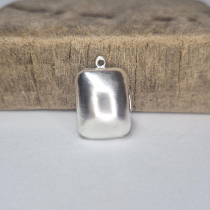 Minimalist rectangular locket in sterling silver photographed standing upright against a rustic wood block.