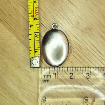 Oval Silver Locket With a Measuring Tape and Ruler for Scale.