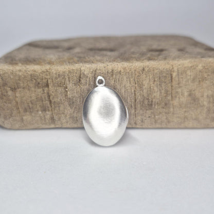 Closed Oval Silver Locket Standing Against a Wooden Block.