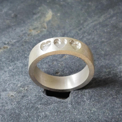 Side profile of a handmade silver memorial ring, highlighting the depth of the three recessed heart shapes.