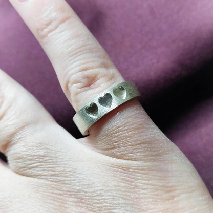 Silver ring with recessed hearts shown upright, emphasizing the smooth interior and textured exterior.