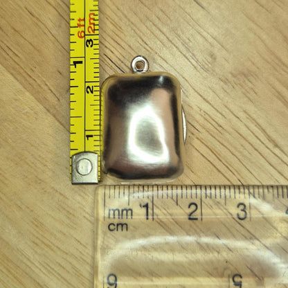Sterling silver rectangular locket placed beside a ruler and measuring tape to show scale in millimetres and inches.