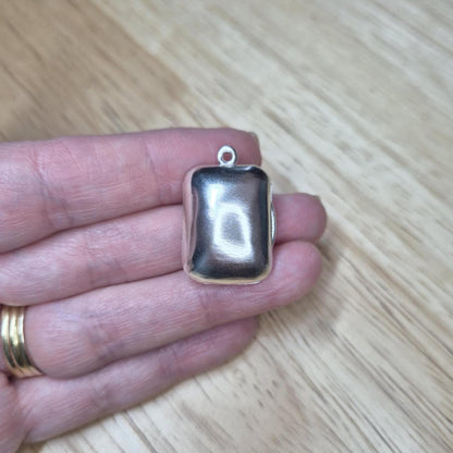Rectangular silver locket held in hand to demonstrate size and smooth polished finish.