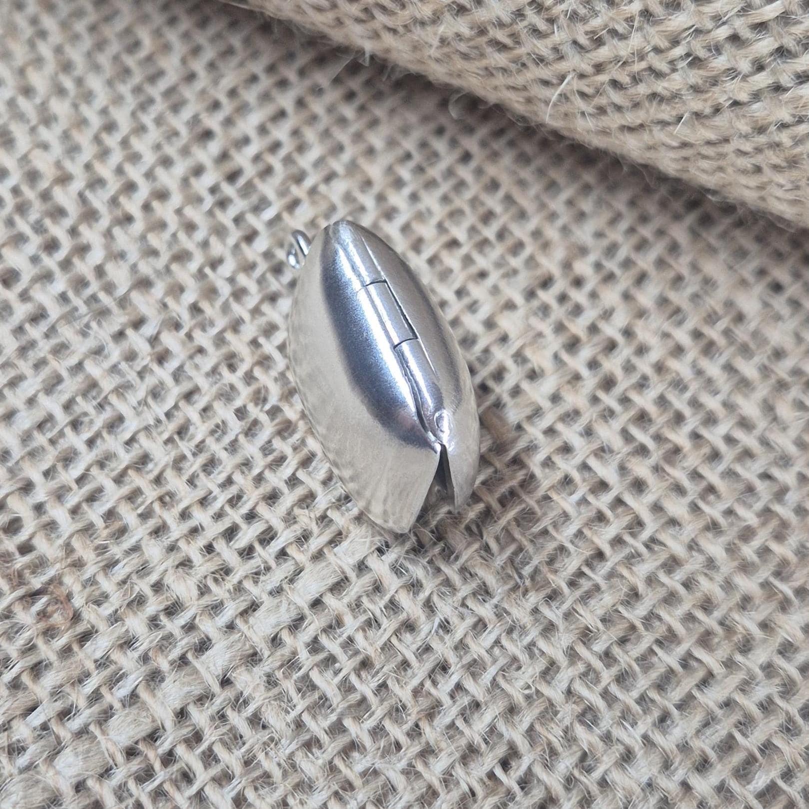 Side profile of rectangular sterling silver locket showing thickness and subtle curve against hessian background.