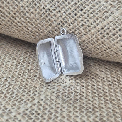 Open sterling silver locket photographed on hessian, showing internal cavities and rounded corners.