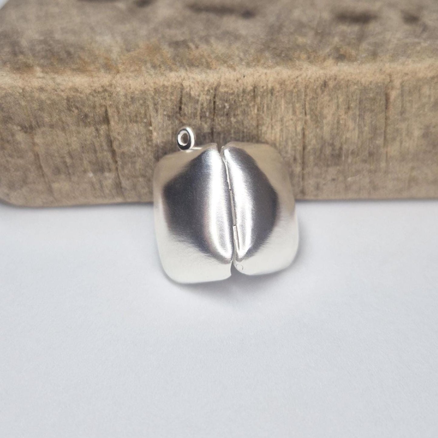 Sterling silver locket closed, viewed from behind against a wood block to show smooth polished back.