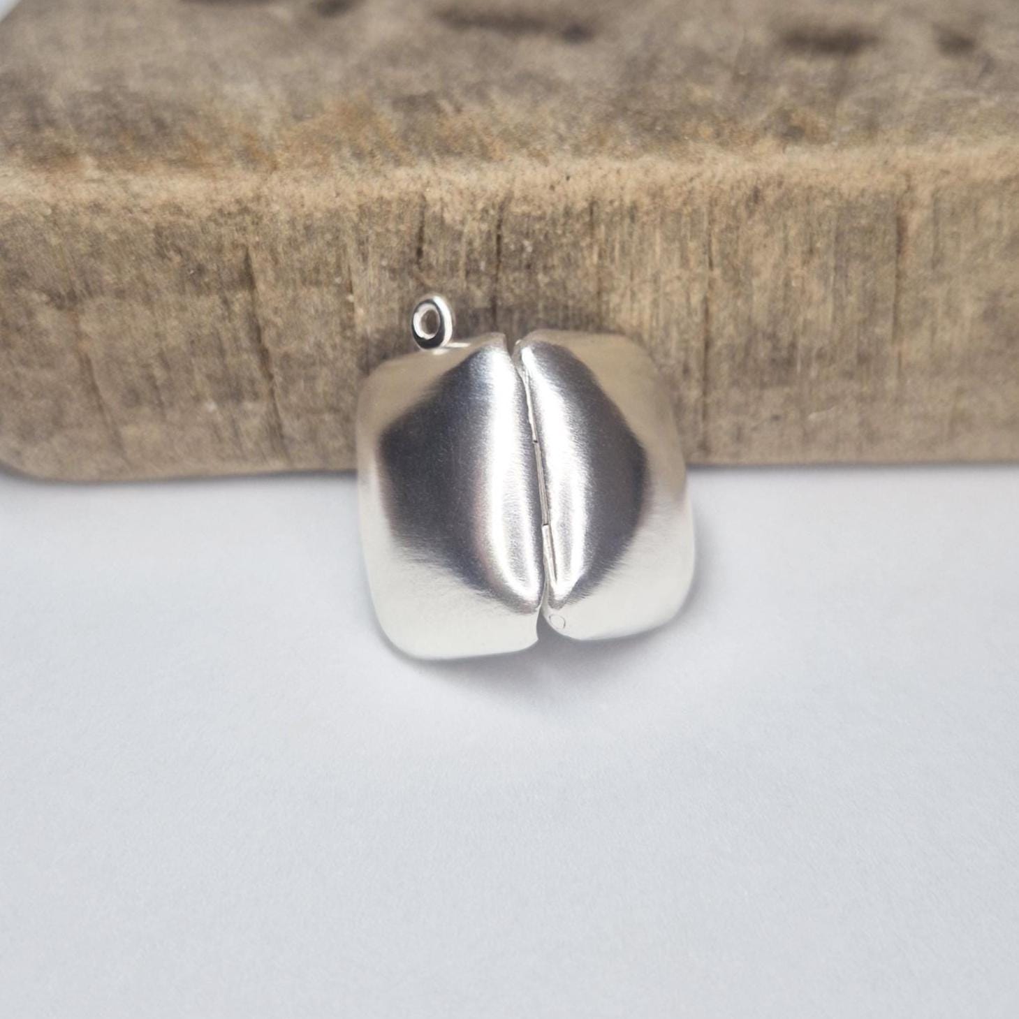 Sterling silver locket closed, viewed from behind against a wood block to show smooth polished back.