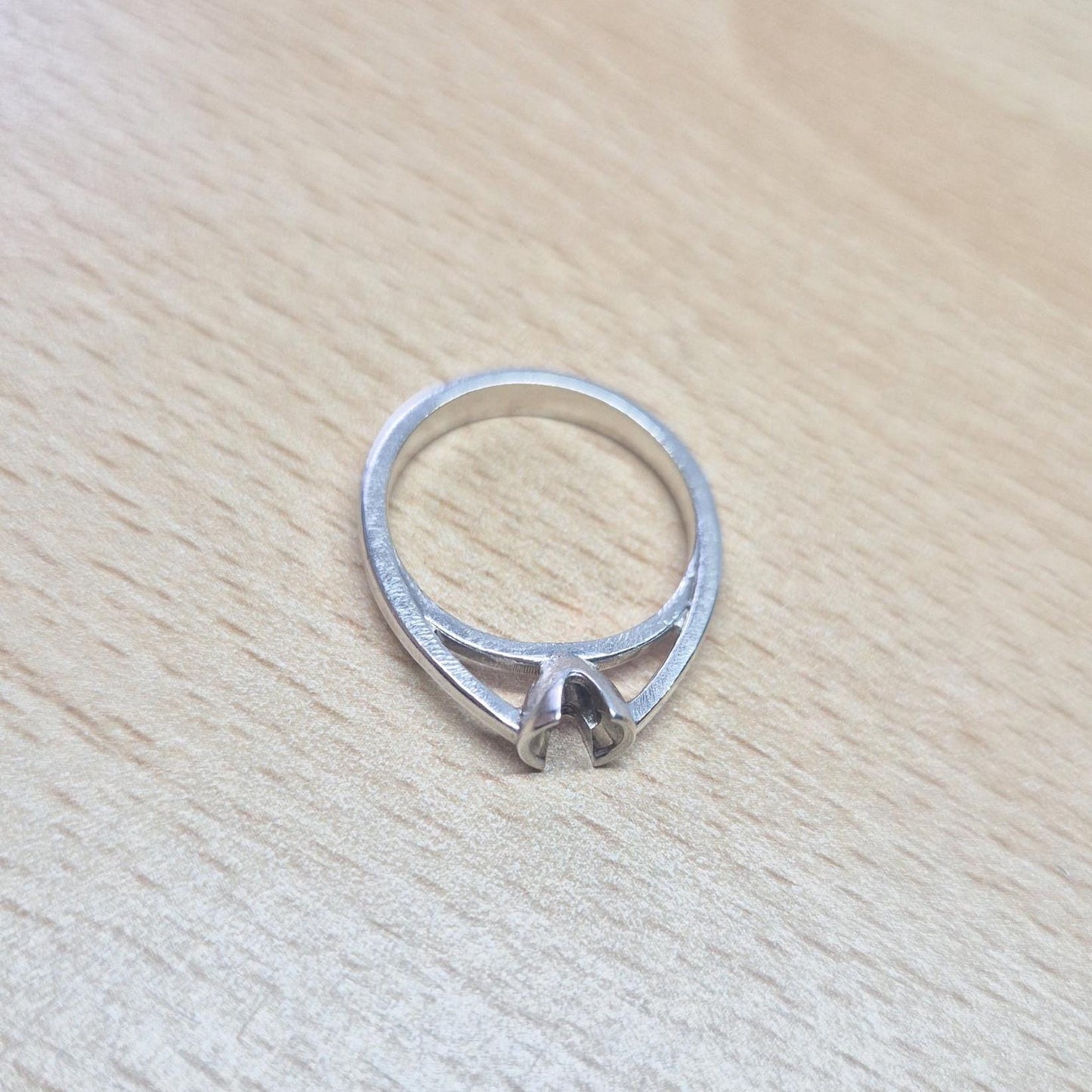 Sterling silver solitaire ring setting placed flat on a wood surface, showcasing its V-prong architecture.