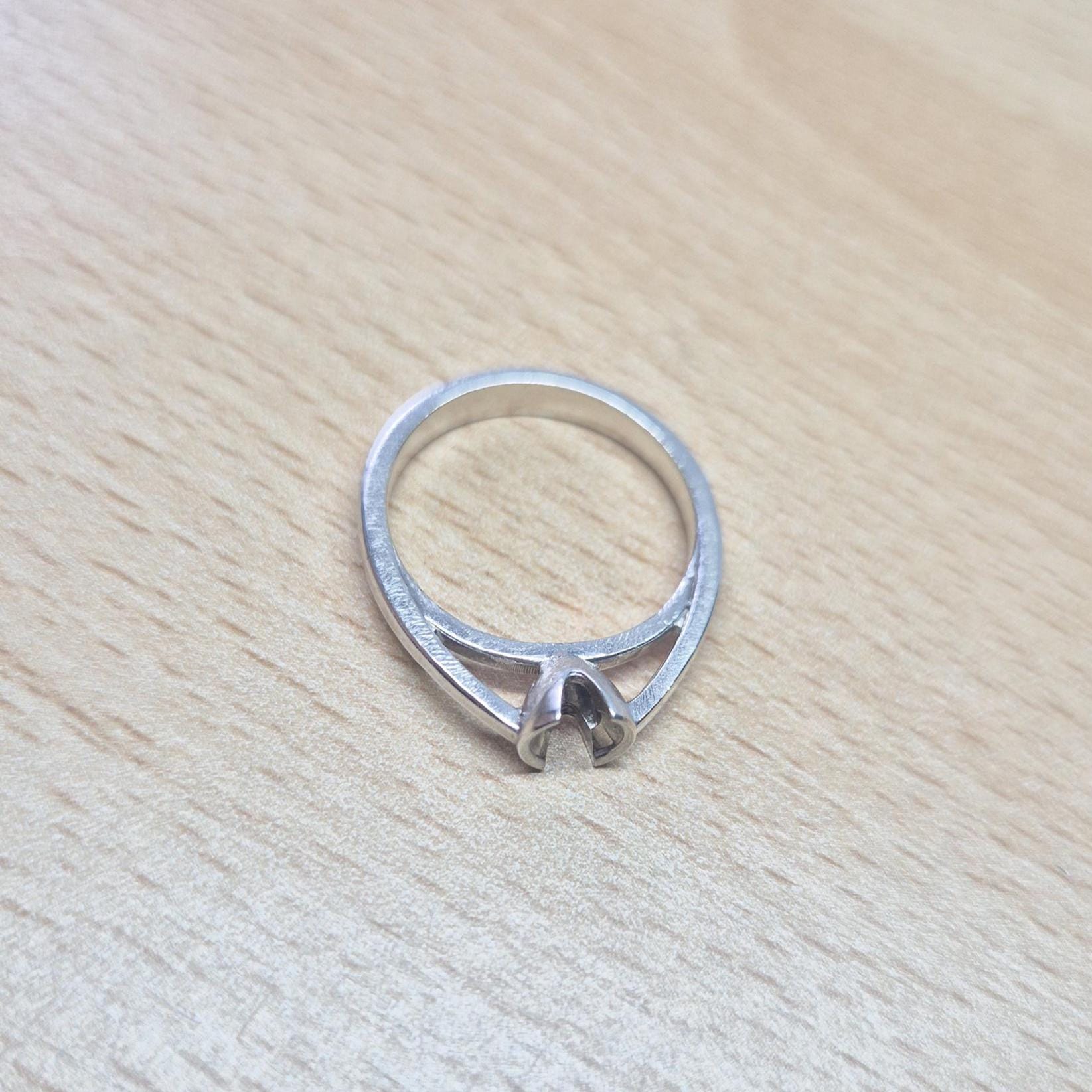 Sterling silver solitaire ring setting placed flat on a wood surface, showcasing its V-prong architecture.