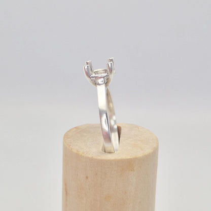 Profile view of a sterling silver ring setting with a four-prong square head, standing upright on a short, wide conical wooden stand, highlighting the elevation of the setting.