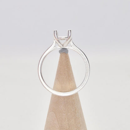 Back view of a sterling silver ring setting with a four-prong square head, displayed on a conical wooden stand, showing the full circle of the band and the open back of the setting.