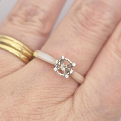 Sterling silver ring setting with a four-prong round head, worn on a hand alongside a plain gold band, providing a real-life perspective of the ring on a finger.