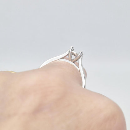 Close-up view of a sterling silver ring setting with a four-prong round head, worn on a hand, showing the detailed construction of the setting from a low angle.