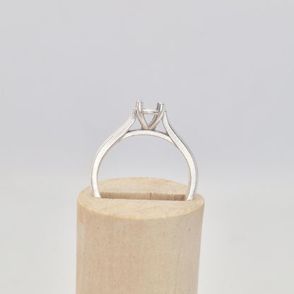 Front view of a sterling silver ring setting with a four-prong round head, displayed on a conical wooden stand, highlighting the elegant shape of the ring's shoulders.